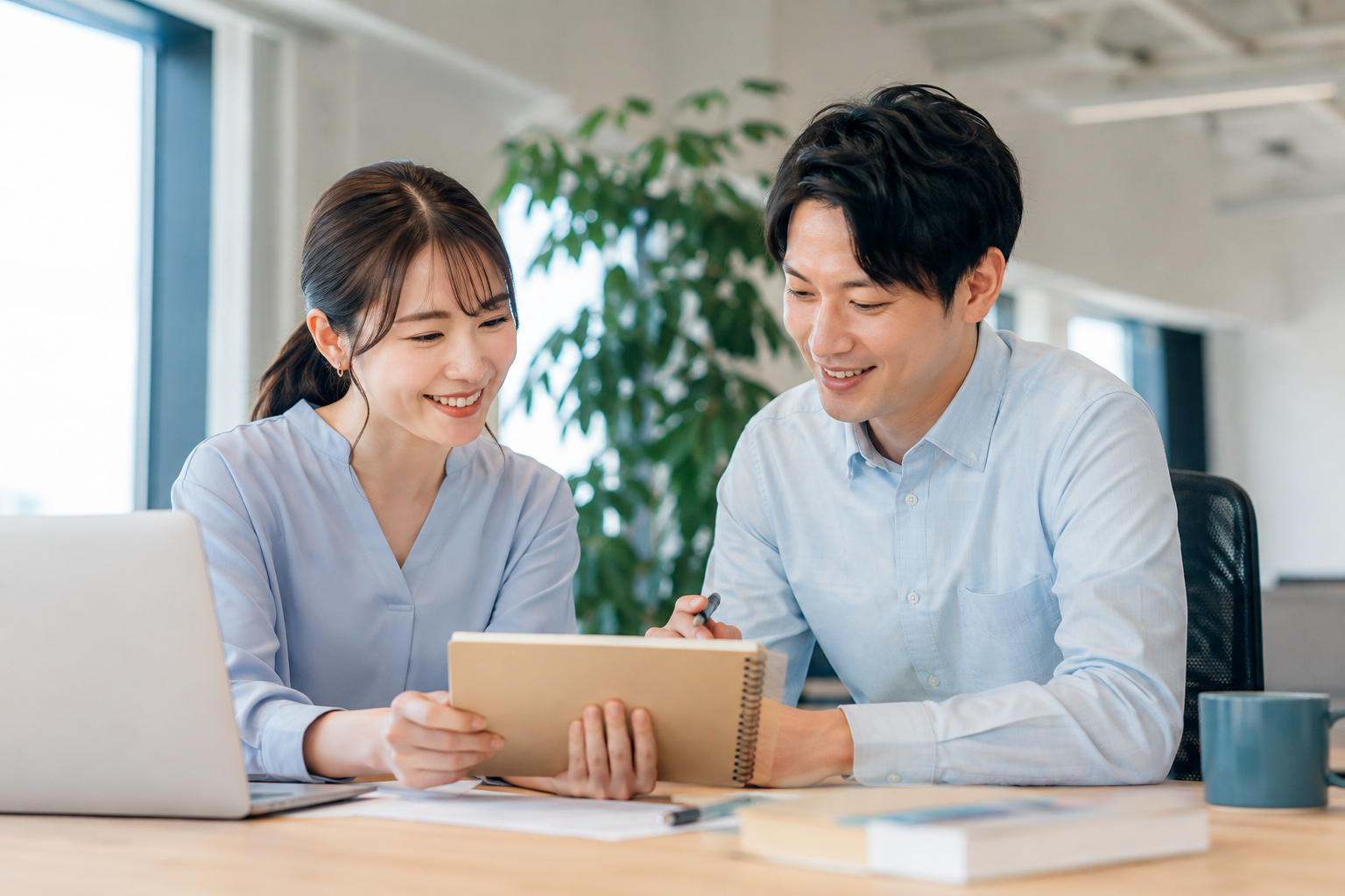 明るいオフィスで、ノートを見ながら相談する同僚たちのイメージ